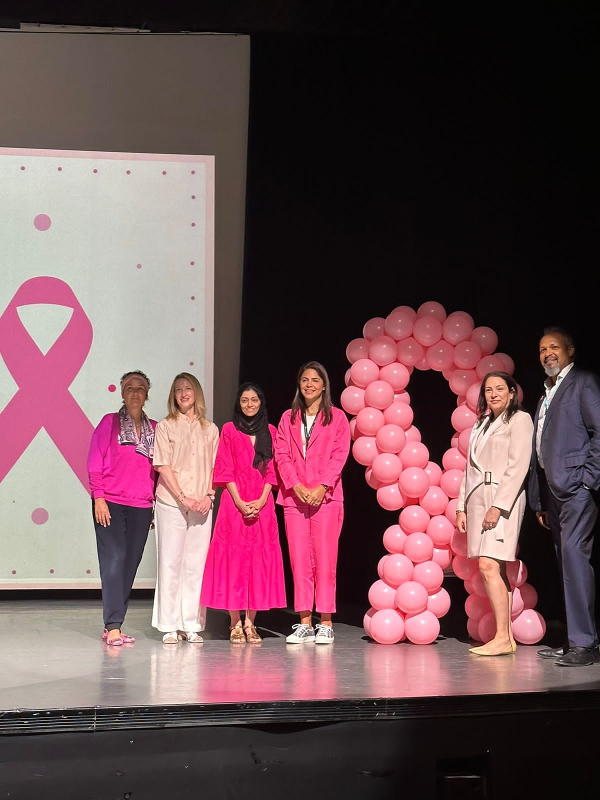 A group standing together on stage beside a tall pink balloon ribbon.